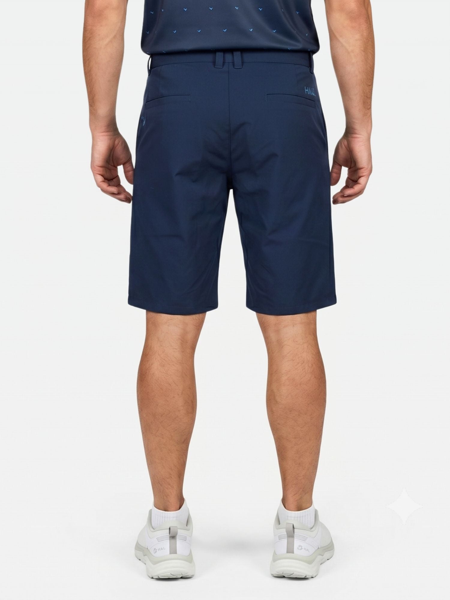 Mies, jolla on yllään Halti Drive X-stretch Shortsit Miesten -shortsit, tumma paita ja valkoiset lenkkarit, seisoo selin kameraan.