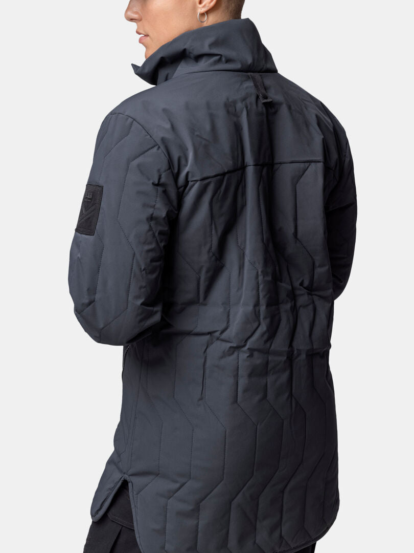 Henkilö pitkässä, tummanharmaassa, korkeakauluksisessa Halti Synkas 3in1 DrymaxX Parka Naisten takapuvussa, takaa kuvattuna.