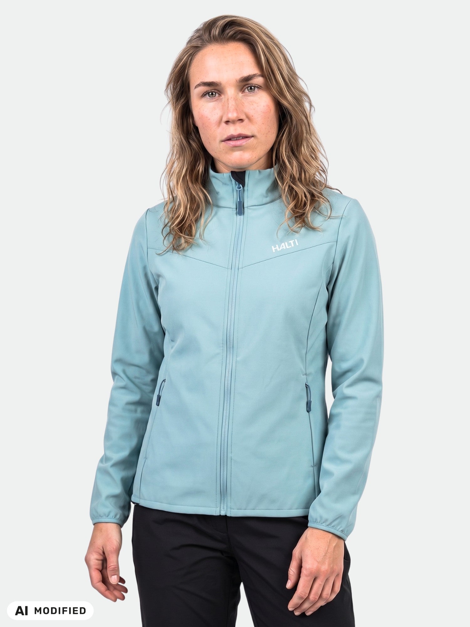 Malli esittelee vaaleansinistä, kierrätysmateriaaleista valmistettua Halti Wedge Softshell-takki Naisten -takkia yksivärisen taustan edessä.
