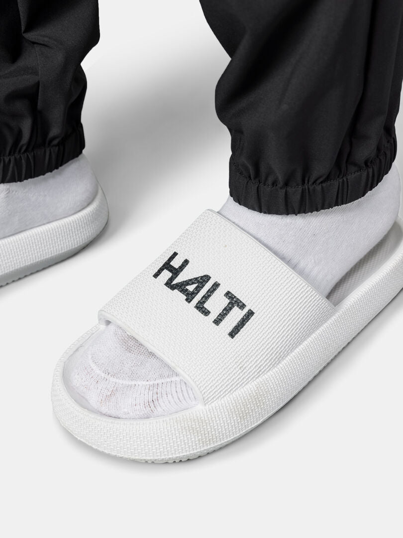 Henkilöllä on yllään valkoiset sukat, valkoiset Halti liukusandaalit ja mustat Halti Grets Joggersit Naisten.