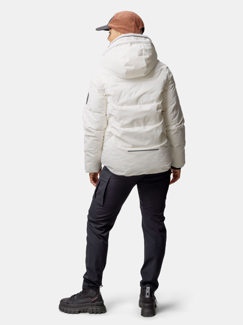 Henkilö, jolla on Halti Brahe Puffer Talvitakki Naisten, mustat housut, saappaat ja ruskea lippis, seisoo kasvot menosuuntaan.