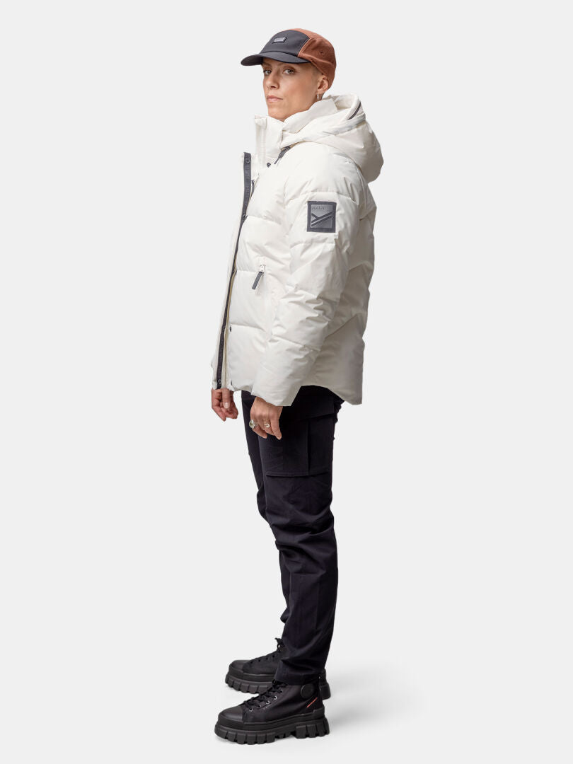 Henkilö seisoo sivuttain Halti Brahe Puffer Talvitakki Naisten, kierrätetystä polyesteristä valmistettu valkoinen hupullinen takki.