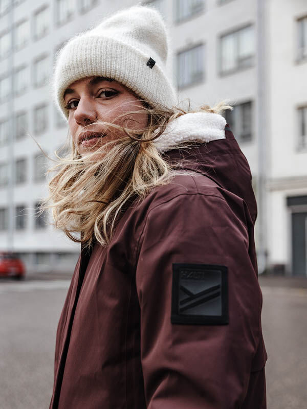 Henkilö, jolla on ruskeankeltainen Halti Tokoi II DX Parkatakki Naisten ja valkoinen neuletakki, seisoo kaupungin kadulla.