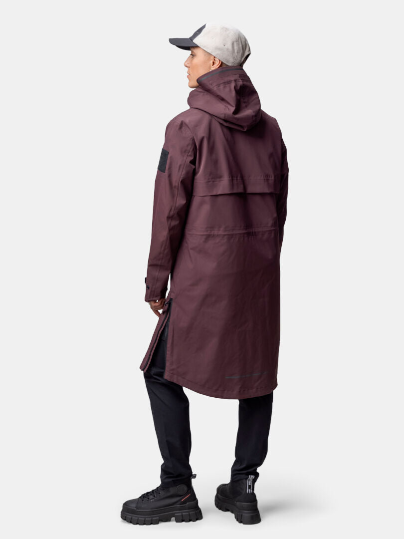 Henkilöllä on yllään ruskeankeltainen Halti Tokoi II DX Parkatakki Naisten, mustat housut ja kengät sekä vaaleanharmaa lippis, kasvot poispäin.