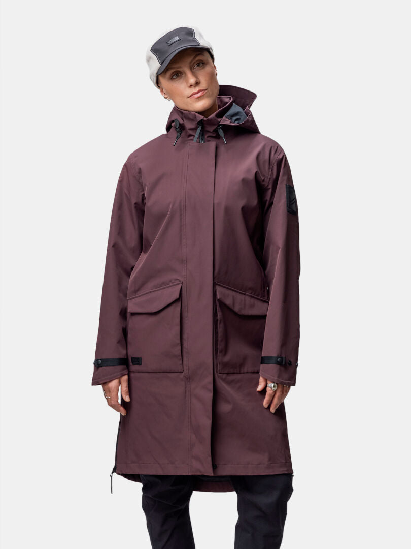 Naisella on ruskeankeltainen Halti Tokoi II DX Parkatakki ja kaksivärinen lippis, kasvot eteenpäin valkoista taustaa vasten.