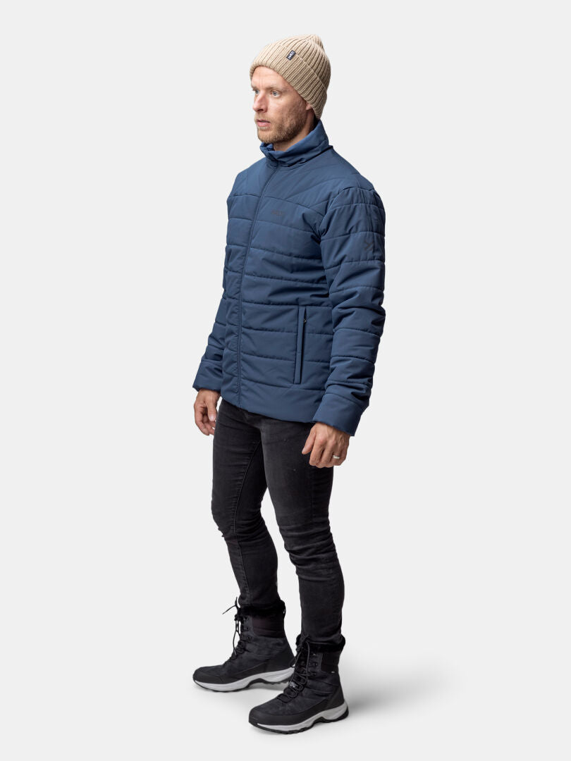Miehellä Halti Haapa Kevyttoppatakki Miesten, beige neulottu pipo, mustat farkut ja saappaat tavallista taustaa vasten.