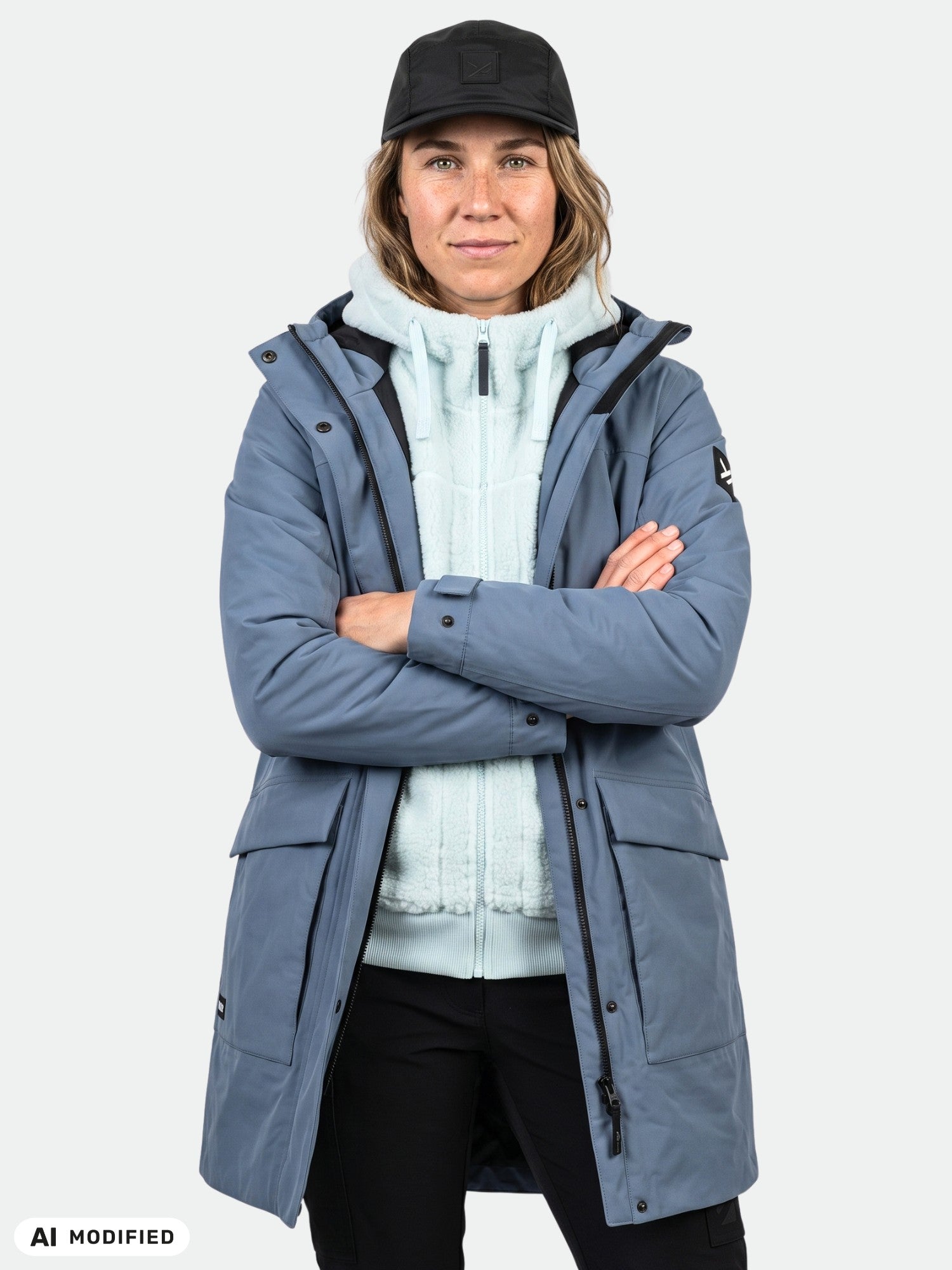 Henkilö, jolla on yllään Halti Kortteli DX -parka, vaalea huppari, mustat housut ja lippalakki, seisoo kädet ristissä yksivärisen taustan edessä.