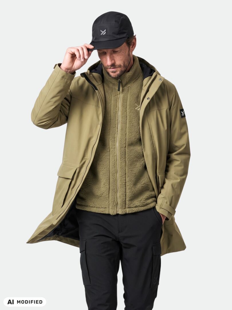 Mies, jolla on yllään Halti Kortteli DX -parka, mustat housut, fleece ja lippalakki; hän katsoo alas ja pitää kiinni lippalakkinsa lieriä.