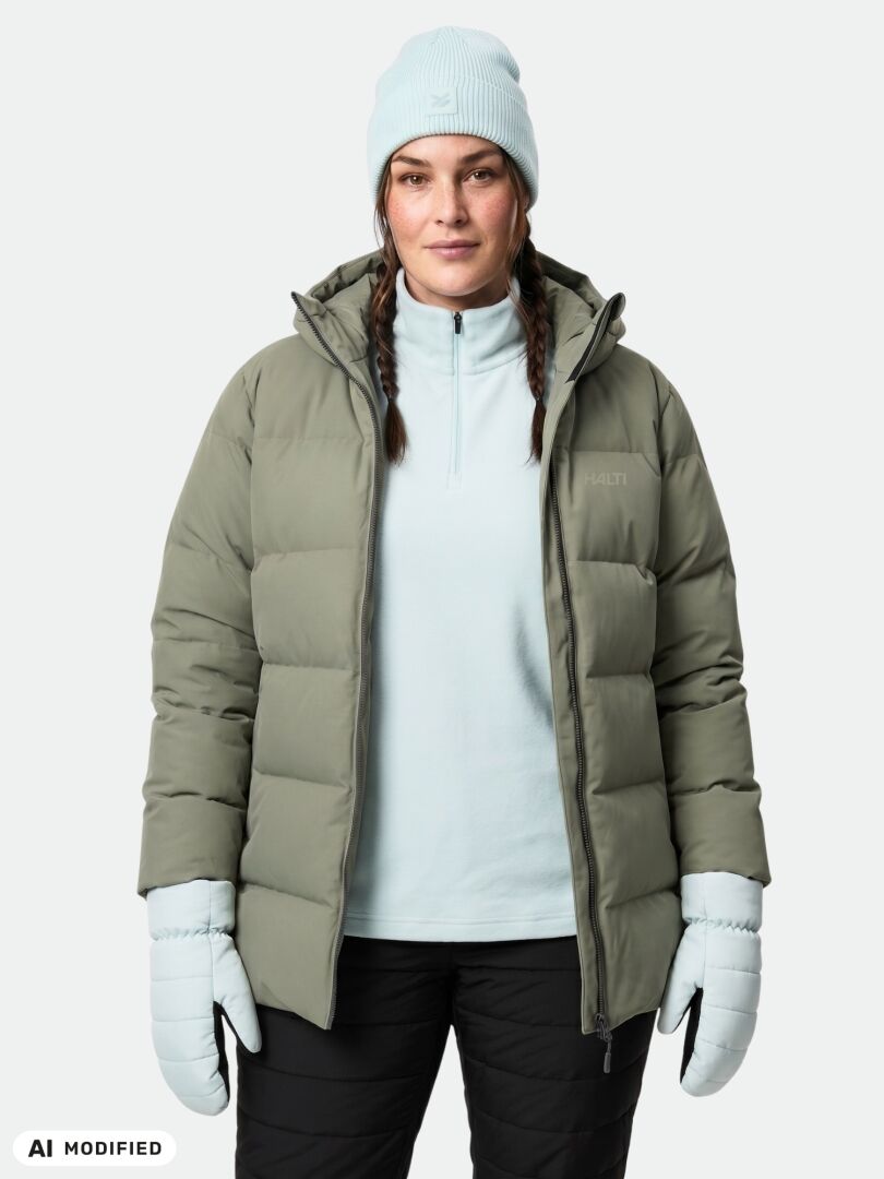 Hänellä on päällään vaaleansininen pipo ja käsineet, ja hän esittelee Halti Leinikko Puffer Parka Naisten Plus -takkia valkoisen paidan päällä.
