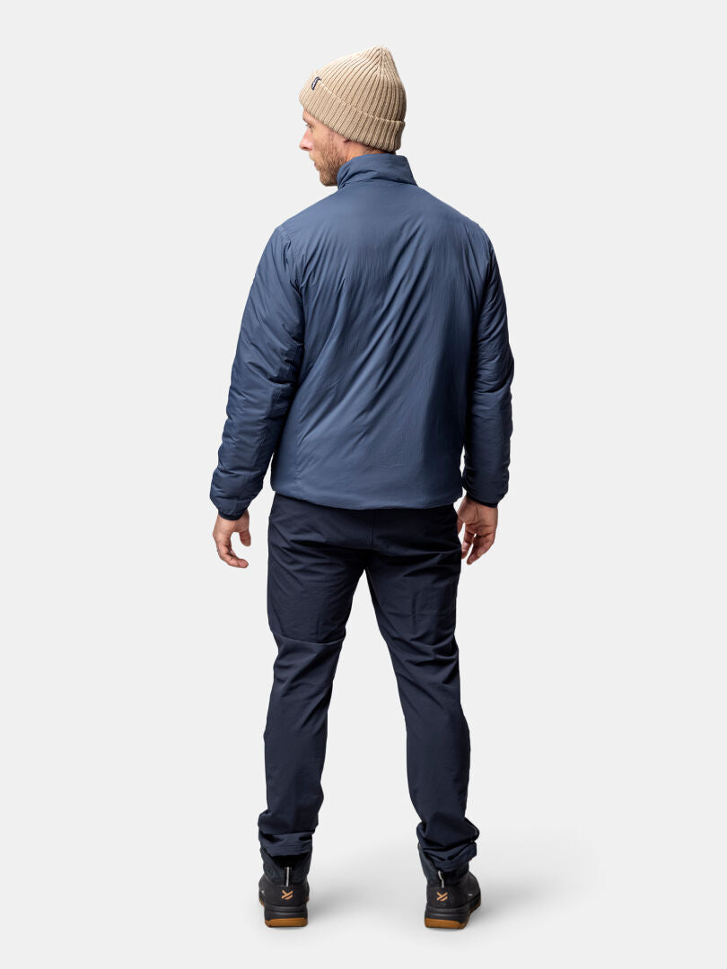 Mies, jolla on beige pipo ja Halti Haave Primaloft Takki, seisoo kasvot menosuuntaan vaaleaa taustaa vasten.