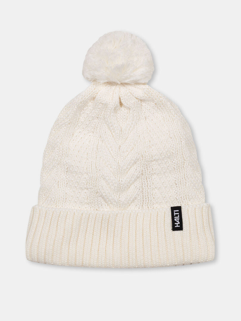 Halti Hile Pipo: valkoinen neuletakki, jossa on pompsut, taitettu lippa, fleecevuori ja musta LIVIN-merkki edessä.