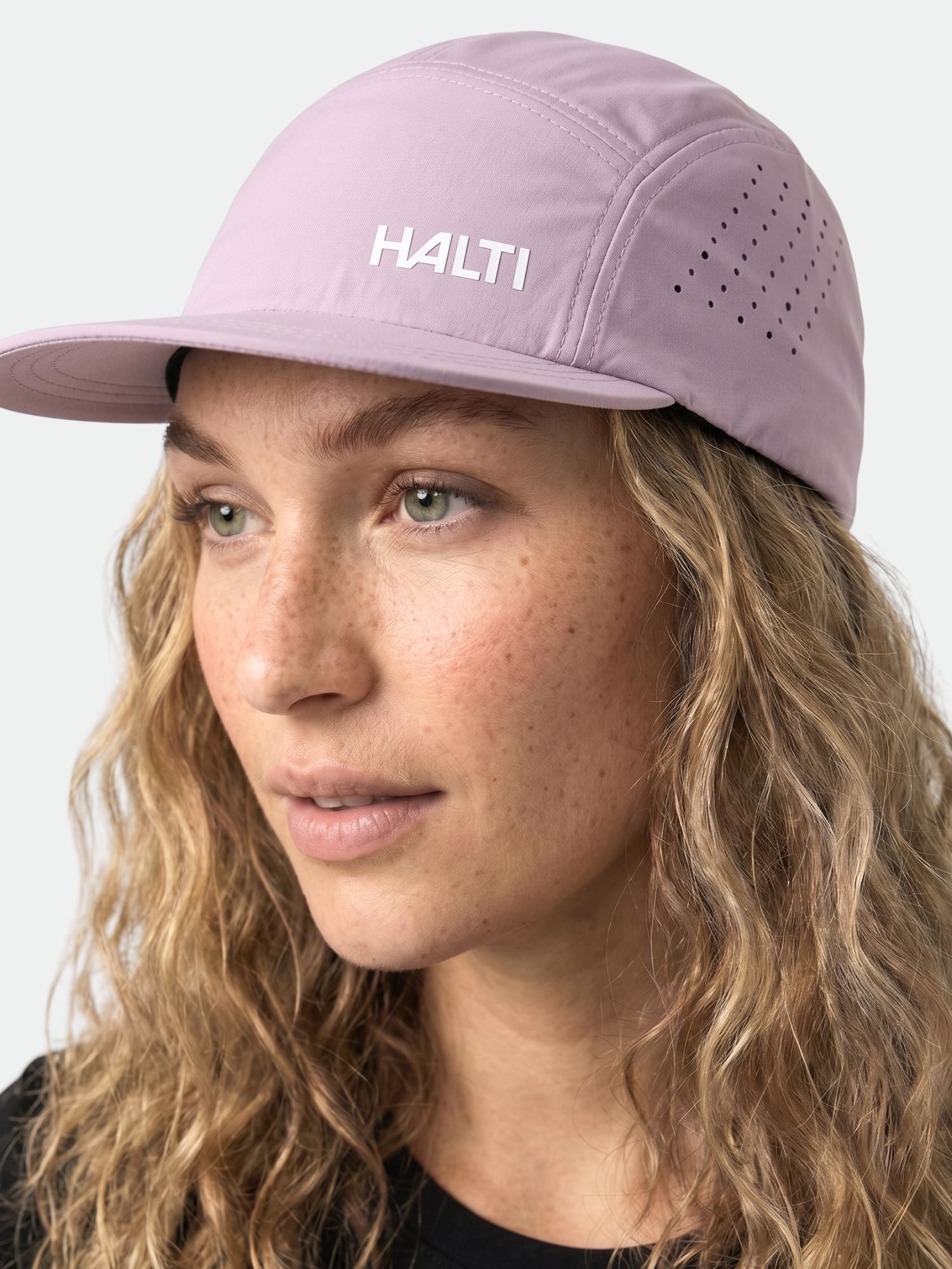 Kiharat vaaleat hiukset omaavalla henkilöllä on päällään vaaleanvioletti Halti Luovi Lippis ja musta paita, katse hieman vasemmalle.