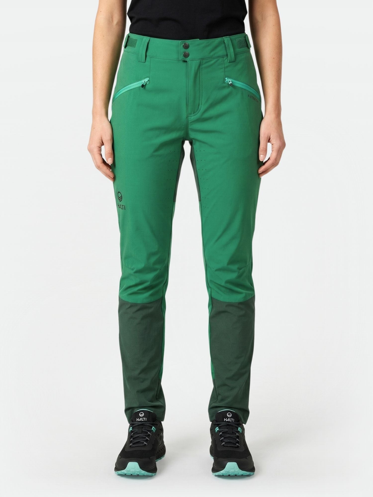 Henkilöllä on yllään Halti Tracks Naisten X-stretch Housut, vihreä, mustat kengät ja musta toppi, kasvot menosuuntaan.