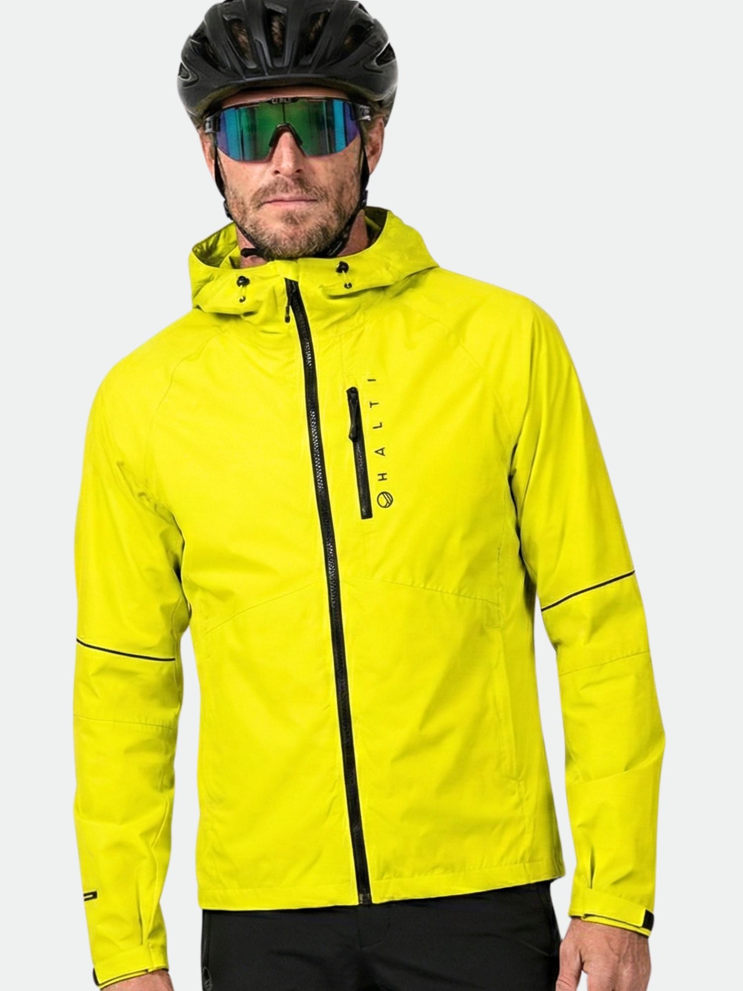 Mies, jolla on keltainen Halti Shelter Stormwall 3L Takki Miesten Takki, musta pyöräilykypärä ja heijastavat aurinkolasit, kasvot menosuuntaan.