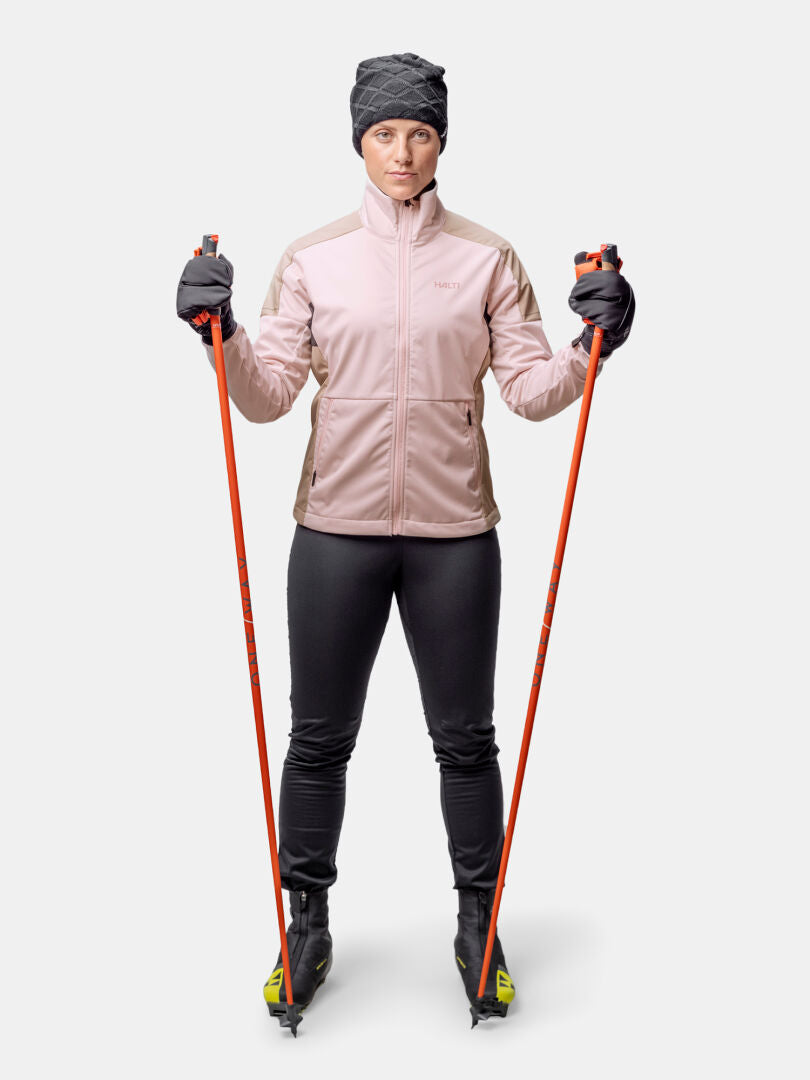 Halti Huuru Maastohiihtopuku Naisten henkilö on valmiina hiihtämään sauvat, saappaat ja talvihattu mukanaan.