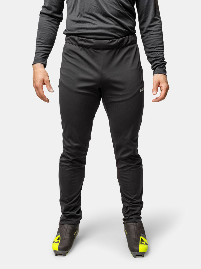 Henkilö, jolla on musta Halti Framover Hiihtohousut Miesten, pitkähihainen paita ja mustat kengät, joissa on keltaiset korostukset, seisoo pystyssä.