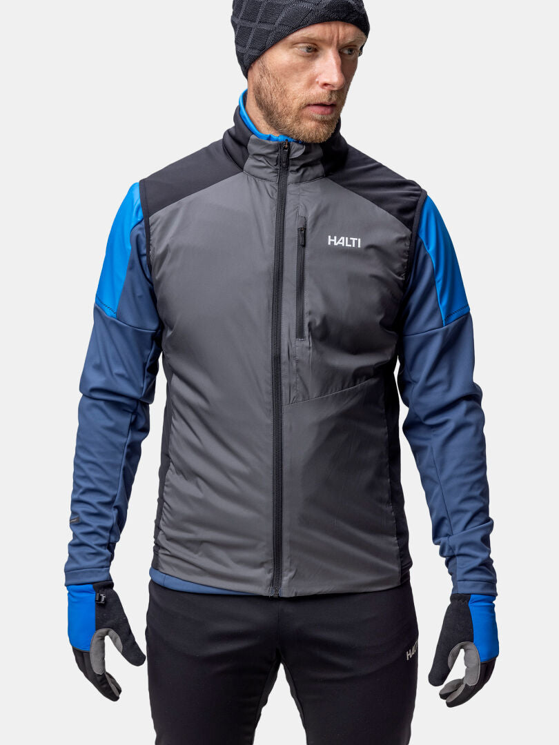 Halti Framover Hiihtoliivi Unisexiin pukeutunut, aktiiviseen urheiluun valmis mies seisoo tavallista taustaa vasten.