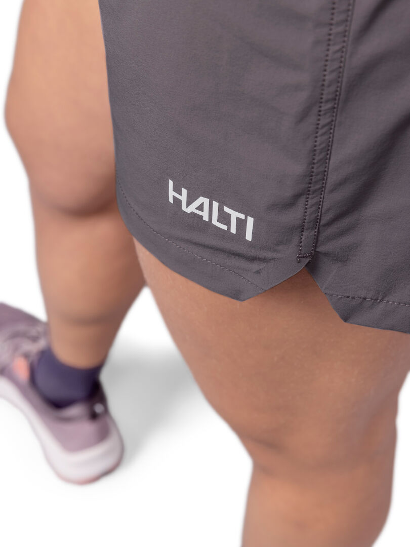 Lähikuva henkilöstä, jolla on harmaat Halti Uurto Shortsit Naisten Active Dry -vaatteet ja violetit lenkkarit, valkoisella pohjalla.