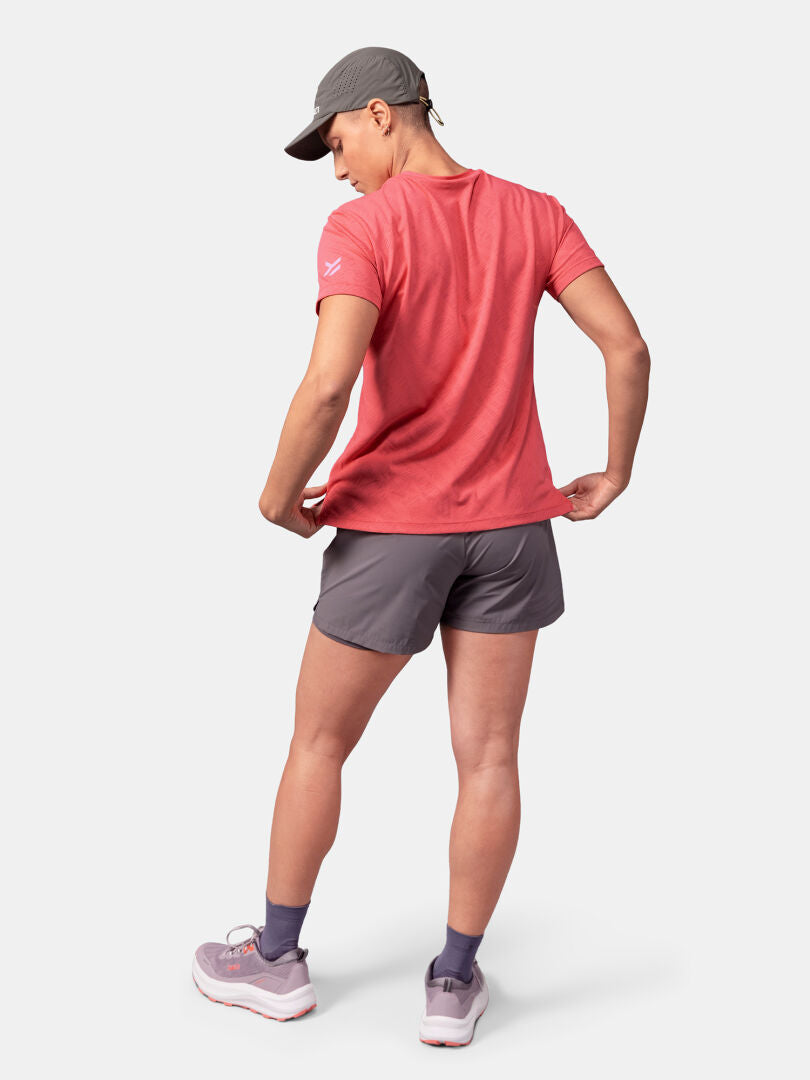 Henkilöllä on yllään punainen Halti Oulanka T-paita Naisten, harmaat shortsit, sukat, lenkkarit ja lippis, kasvot poispäin kamerasta.