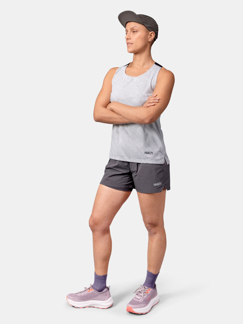 Henkilö seisoo kädet ristissä, yllään Halti Oulanka Treenitoppi Naisten, shortsit, sukat, lenkkarit ja lippis.