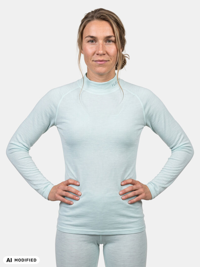 Nainen, jolla on yllään vaaleansininen, pitkähihainen, korkeakauluksinen Halti Neva Merino Kerrasto Naisten -aluspaita.