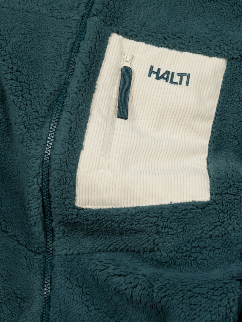 Lähikuva Halti Lumista Polar Fleecetakki Naisten -takista: sinivihreä fleece, jossa on valkoinen vetoketjullinen rintatasku ja brodeerattu logo.